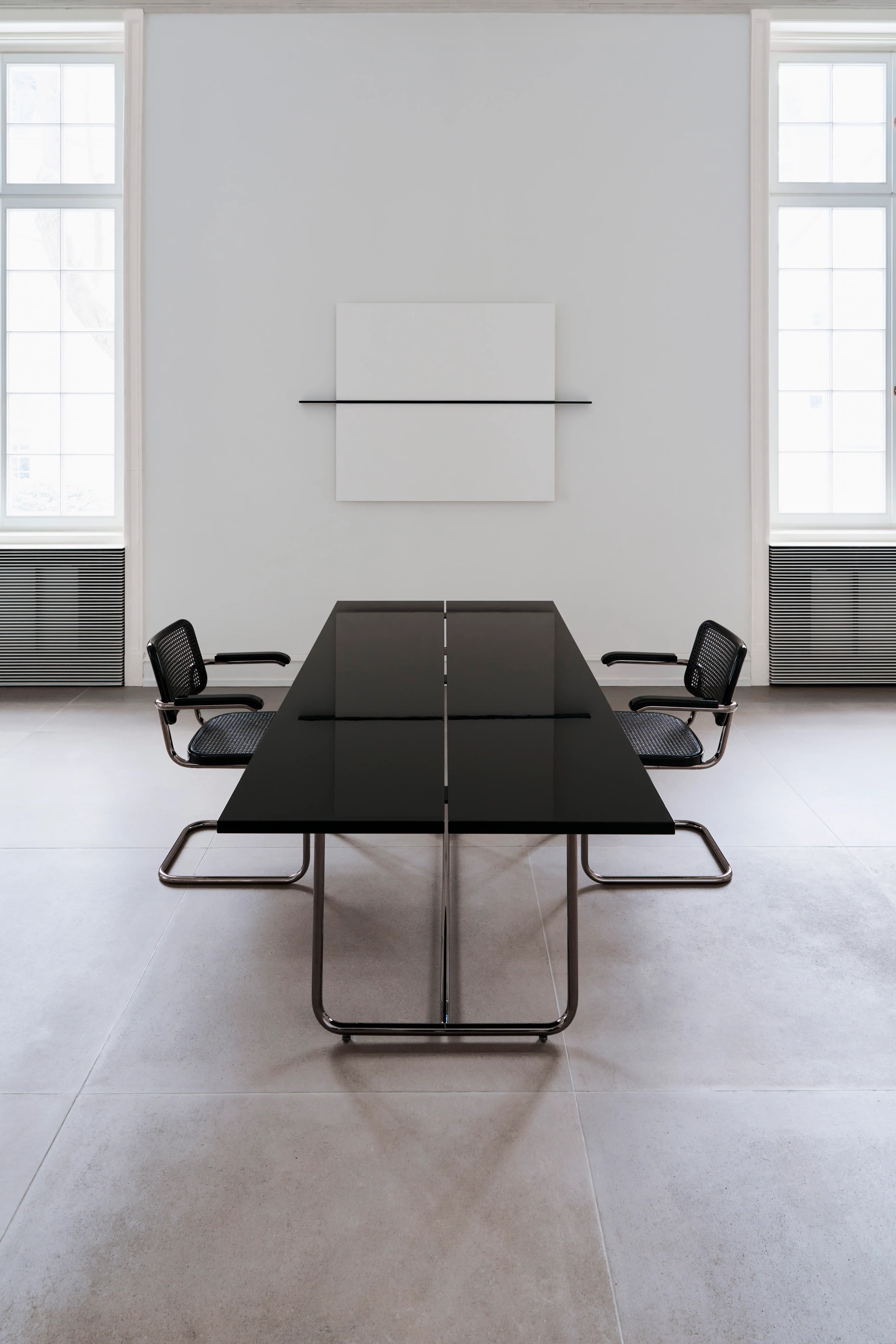 Editorial image for JS . THONET: Thonet S 64 cantilever chairs with black mesh and chrome-plated tubular steel frame, arranged around a large black conference table (S 1070) in a minimalist, light-filled room.
