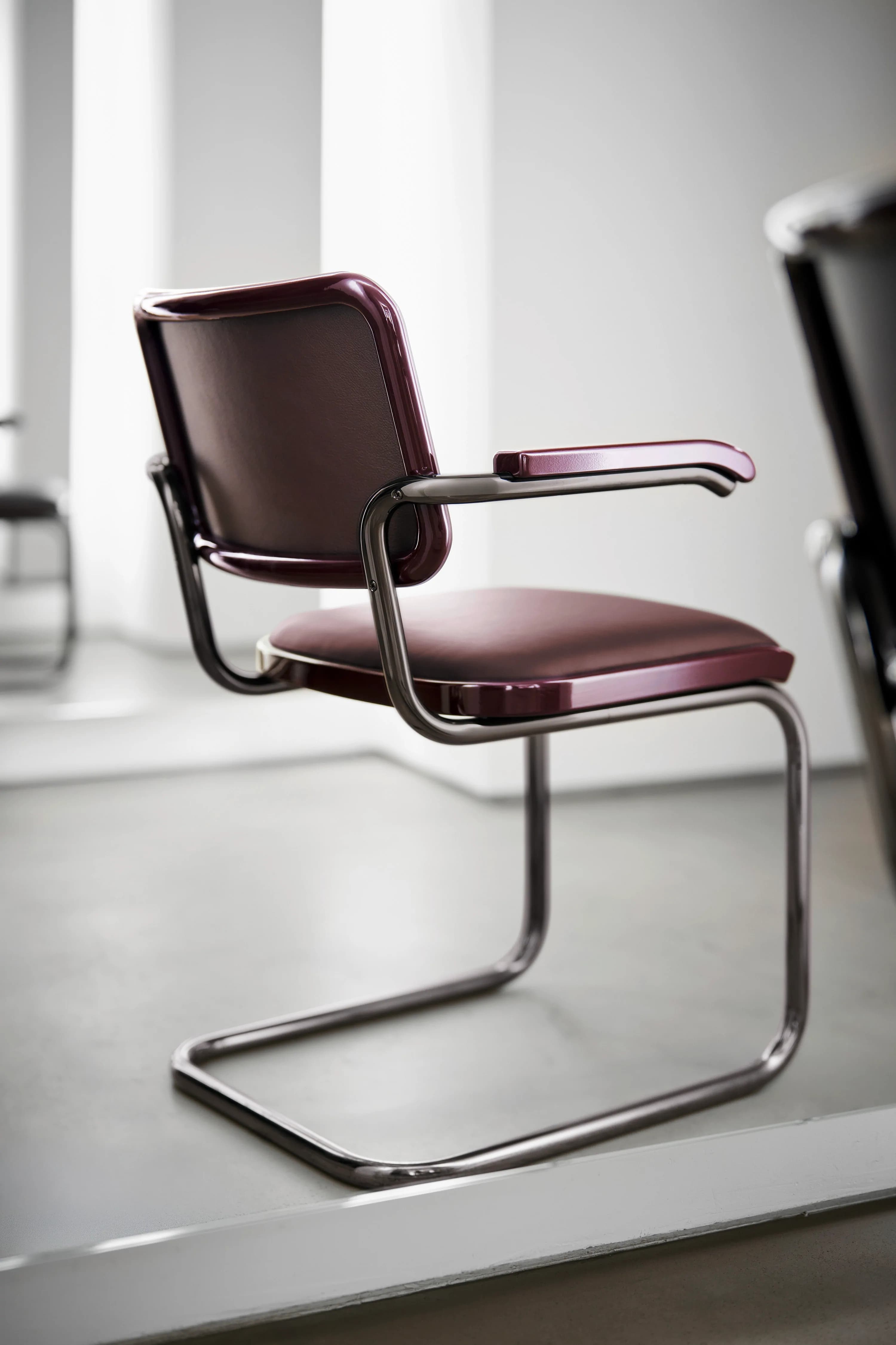 Editorial image for JS . THONET: Thonet S 64 P cantilever armchair in Ruby Red – padded seat and back in bordeaux red leather, chrome-plated tubular steel frame, in a minimalist, light-filled room.