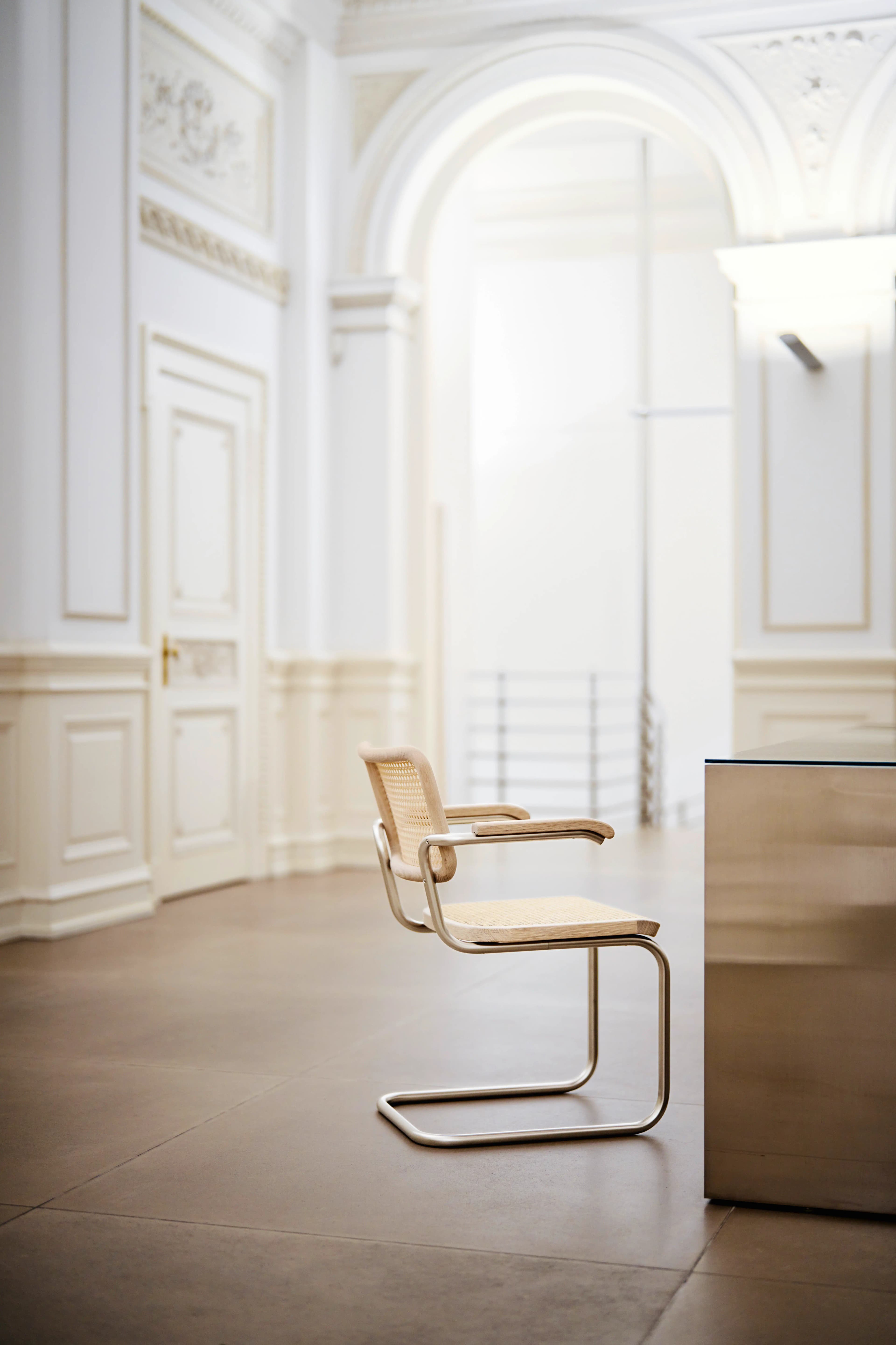 Editorial image for JS . THONET: Thonet S 64 cantilever chair with cane seat and backrest beside a table in a bright room.