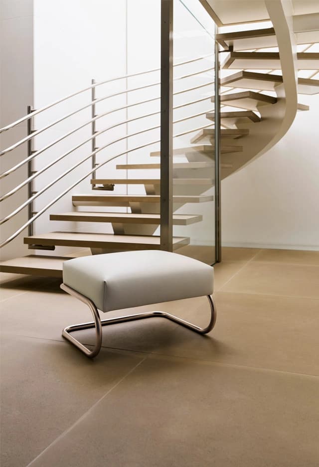 Editorial image for JS . THONET: S 411 H ottoman with leather upholstery in front of a curved staircase.