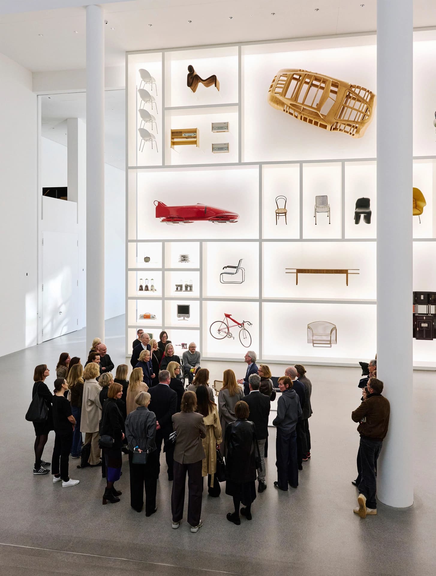 Group of visitors in a museum gallery facing a large wall display of design objects.
