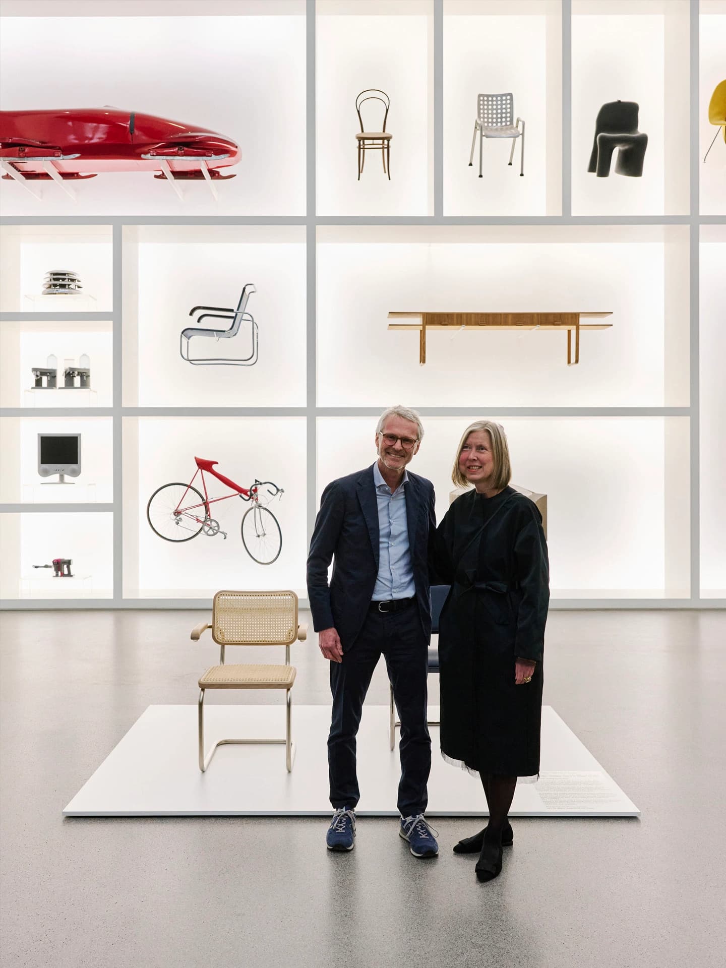 Two people standing next to a display platform with a Thonet cantilever chair in a museum gallery.