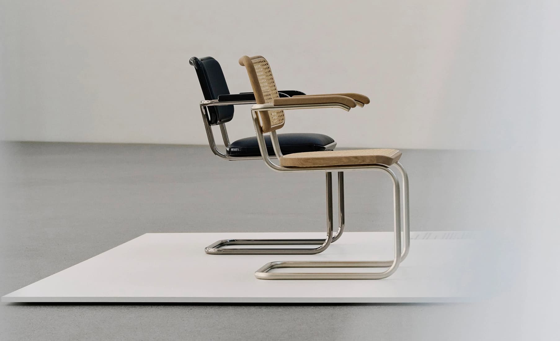 Two Thonet S 64 SERIOUS cantilever chairs displayed on a platform, one upholstered in leather and one with cane seat and backrest.